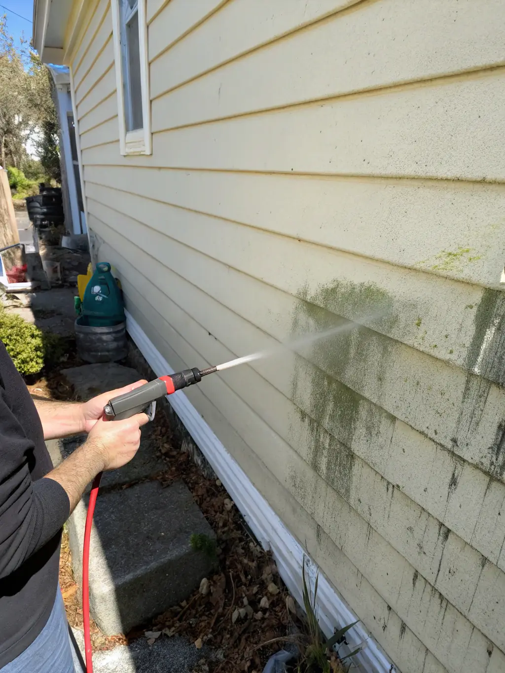 A residential house being soft washed, with visible mold and dirt being removed from the siding, showcasing the effectiveness of the house soft wash service.